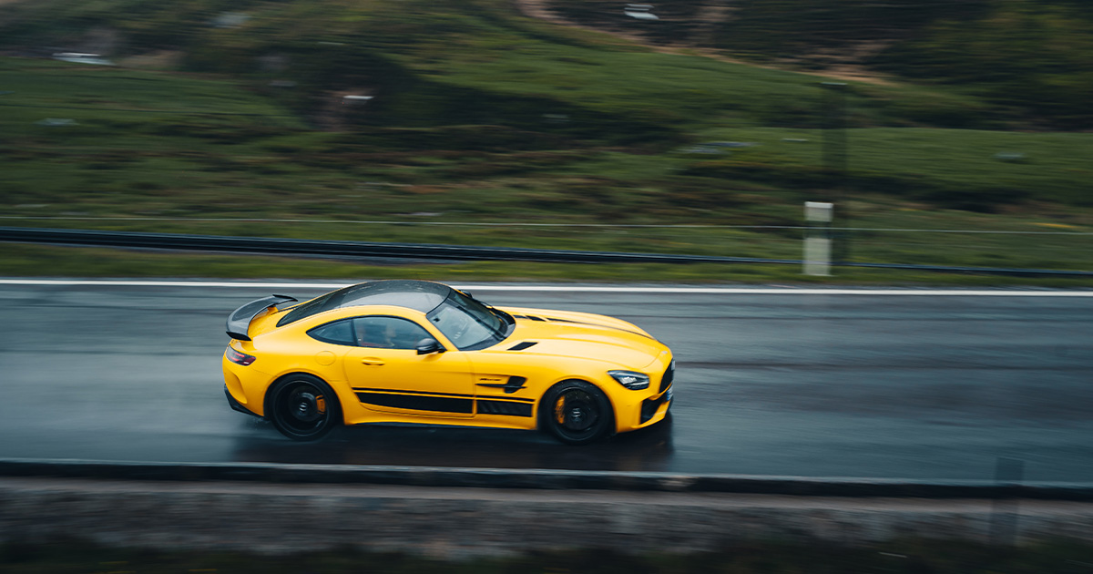 A yellow Mercedes AMG GT making quick progress on a wet stretch of country road