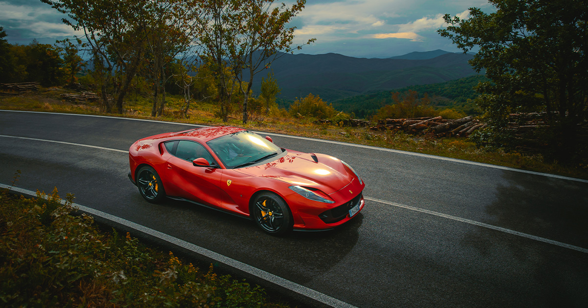 A red Ferrari 812 Superfast rounds a corner on a country road.