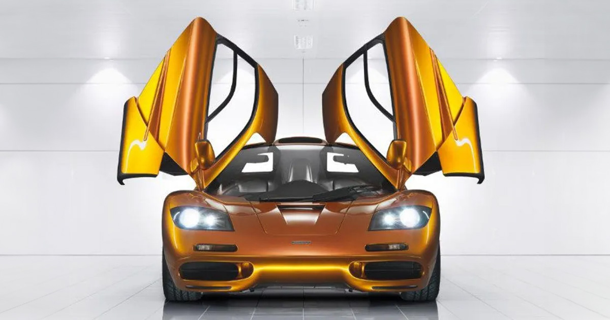 A metallic orange McLaren F1 with its dihedral doors open to the sky and its headlights on