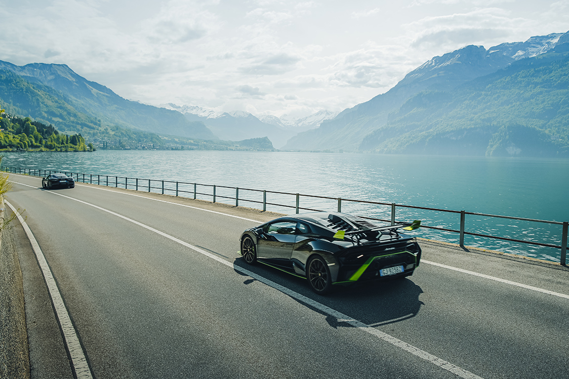 A black Lamborghini Huracan passes by a beautiful lake in the mountains on a European supercar tour