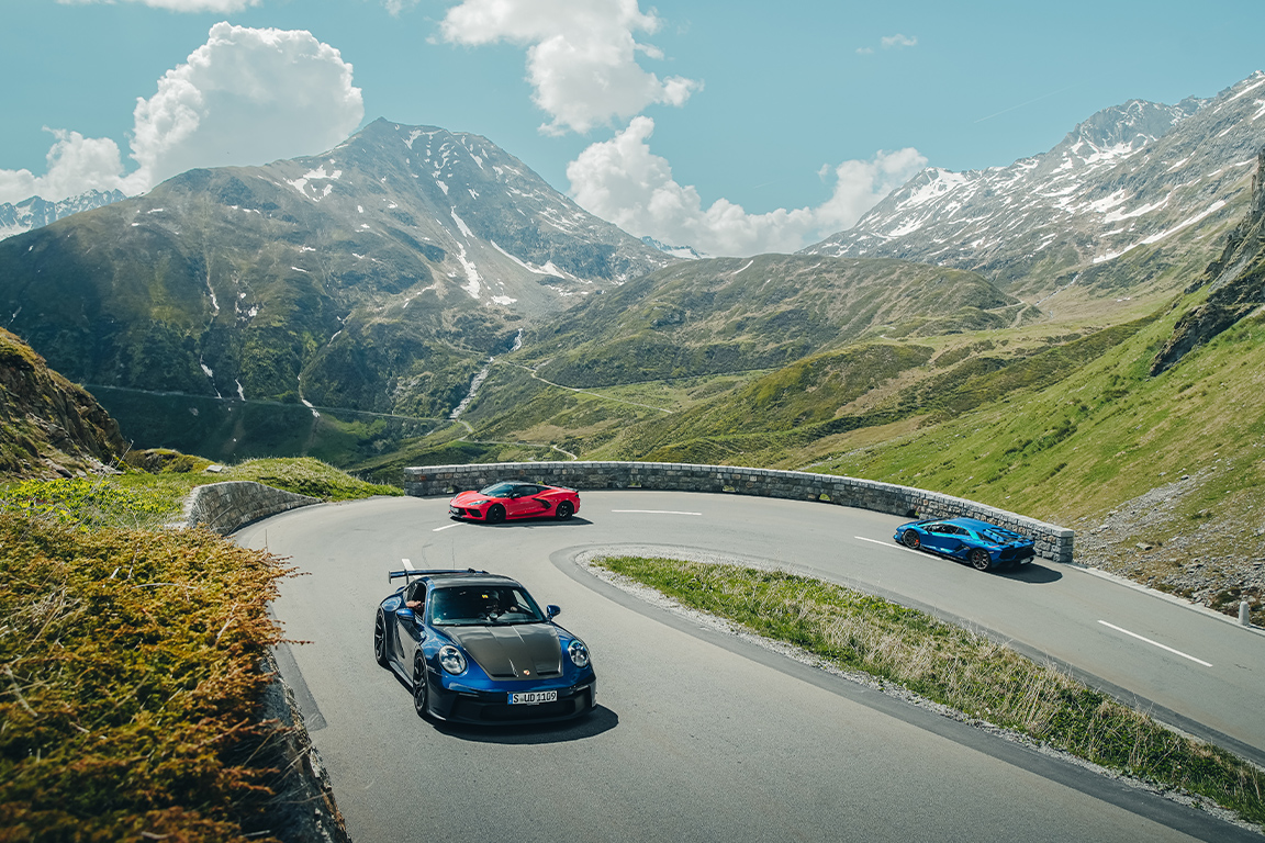 Convoy of supercars turning a corner on an alpine road in Europe on a luxury driving tour