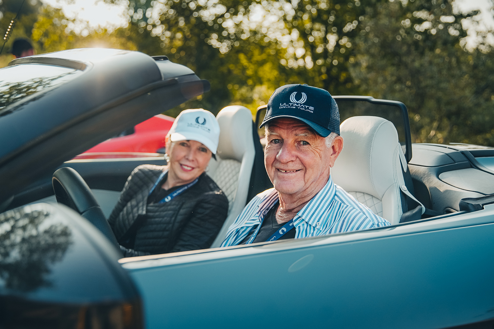 A happy couple wearing Ultimate Driving Tours branded baseball caps as they drive their convertible supercar