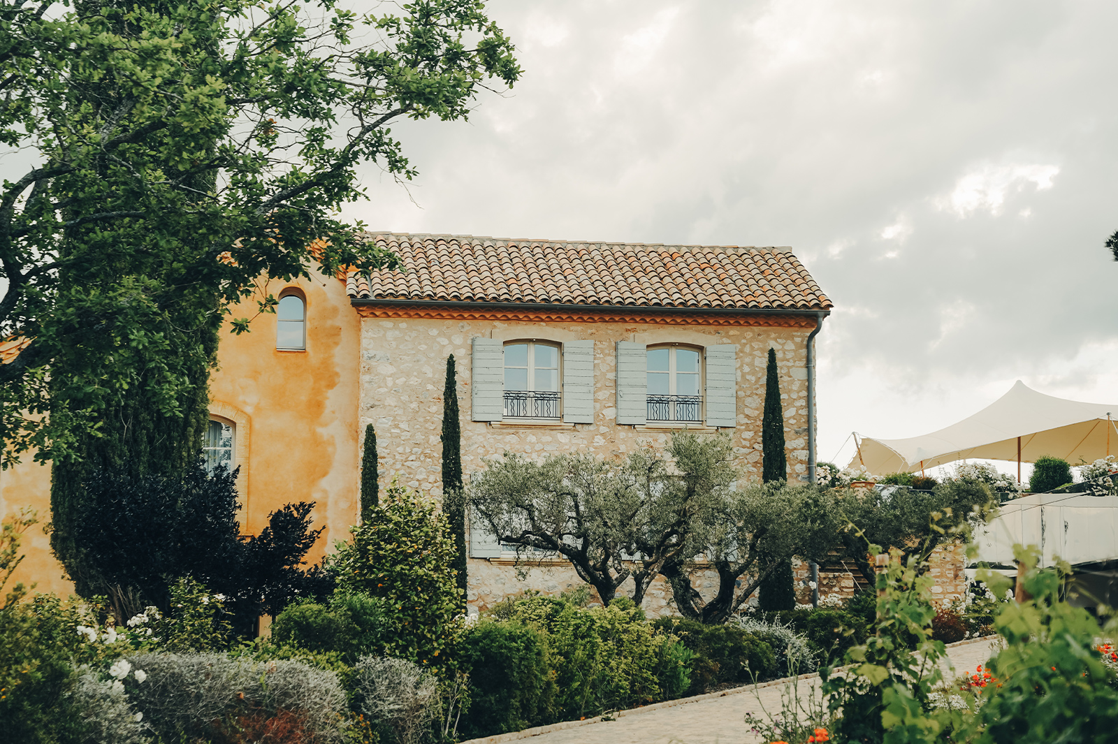 A yellow stone European villa with clay roof tiles and timber window shutters seen on a cloudy day