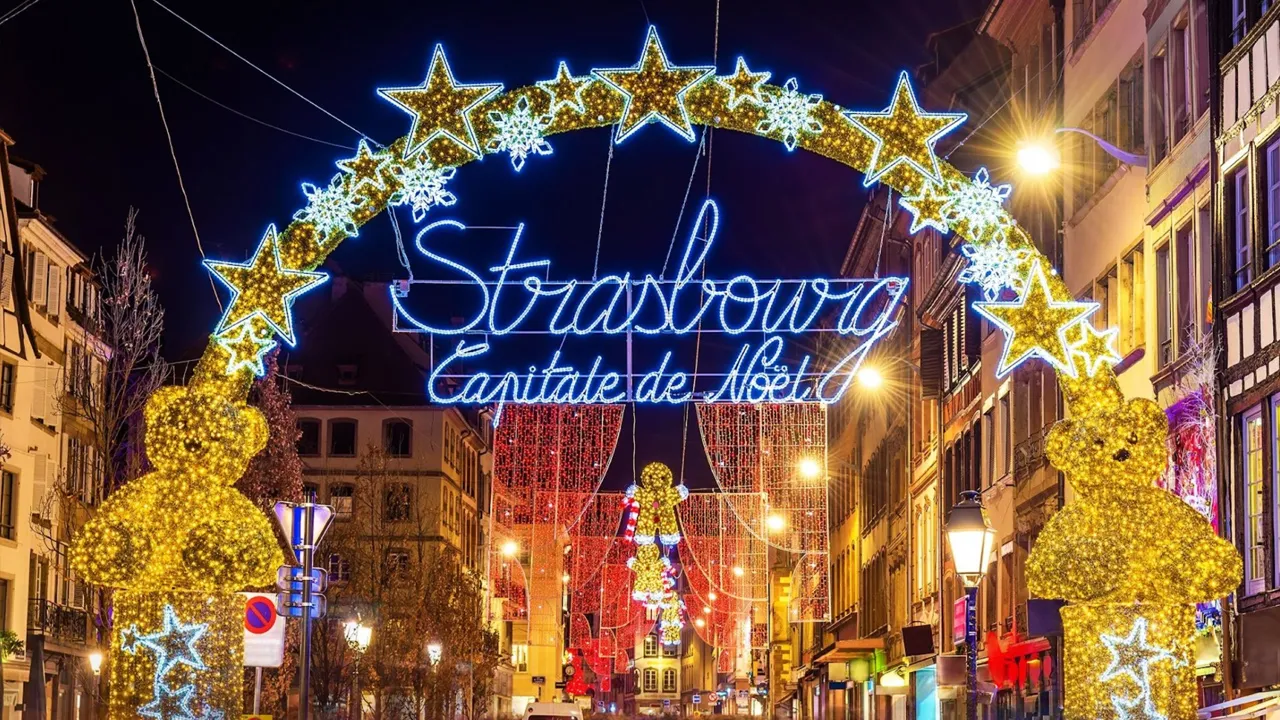 A neon sign with stars acting as an archway through a street filled with Christmas lights in Strasbourg, France