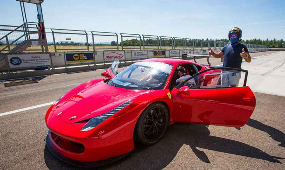 A track-ready red Ferrari is prepared to be driven round the Monza circuit by one of Ultimate Driving Tours’ guests. He has two thumbs up.