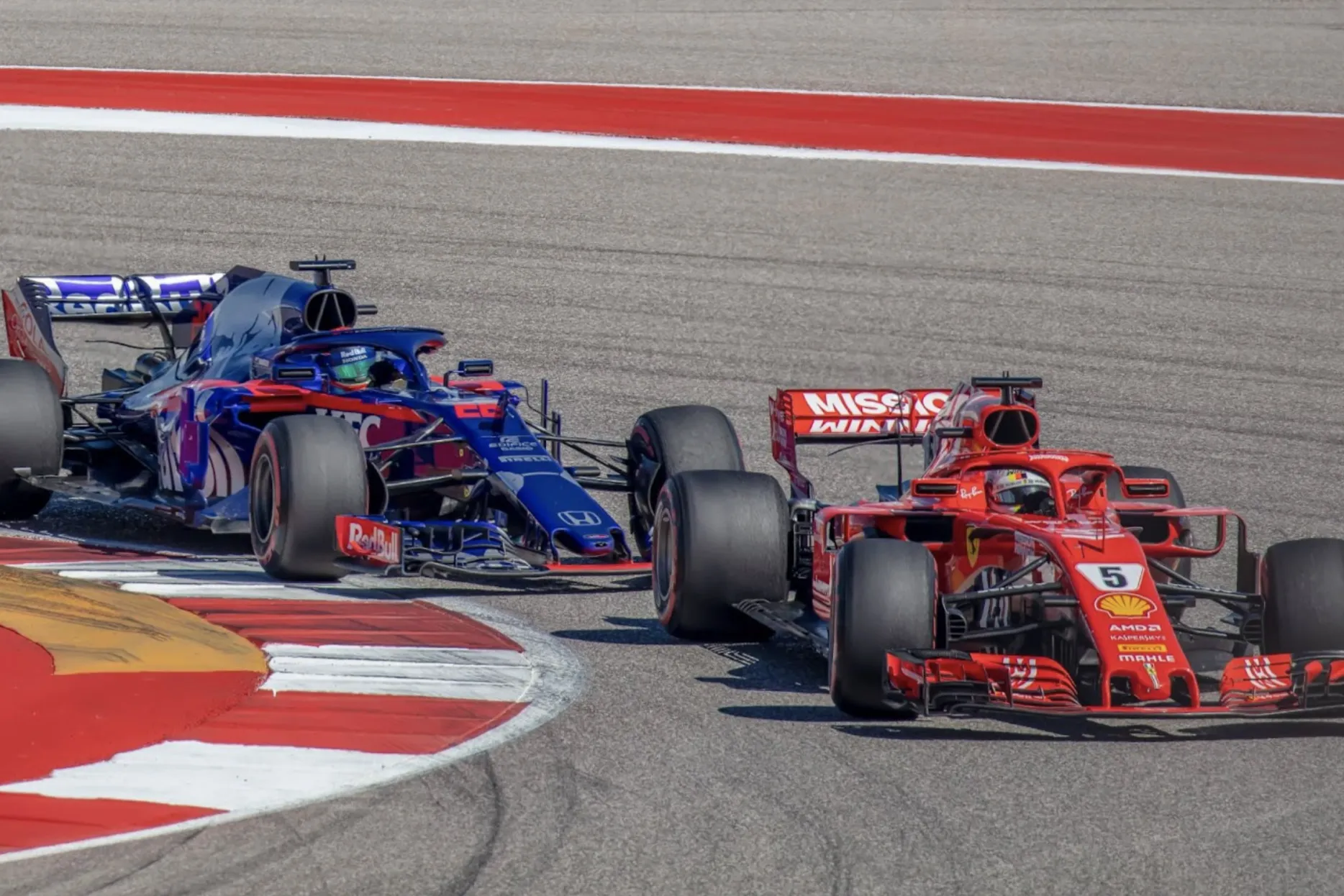 A Red Bull Racing F1 car closely tails a Ferrari F1 car as they round a corner at the Austin Grand Prix