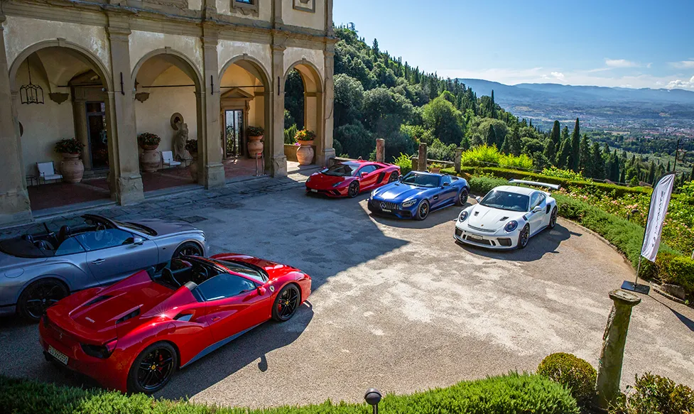 The Ultimate Driving Tours fleet of supercars sits outside a quintessential Tuscan luxury villa on a sunny day