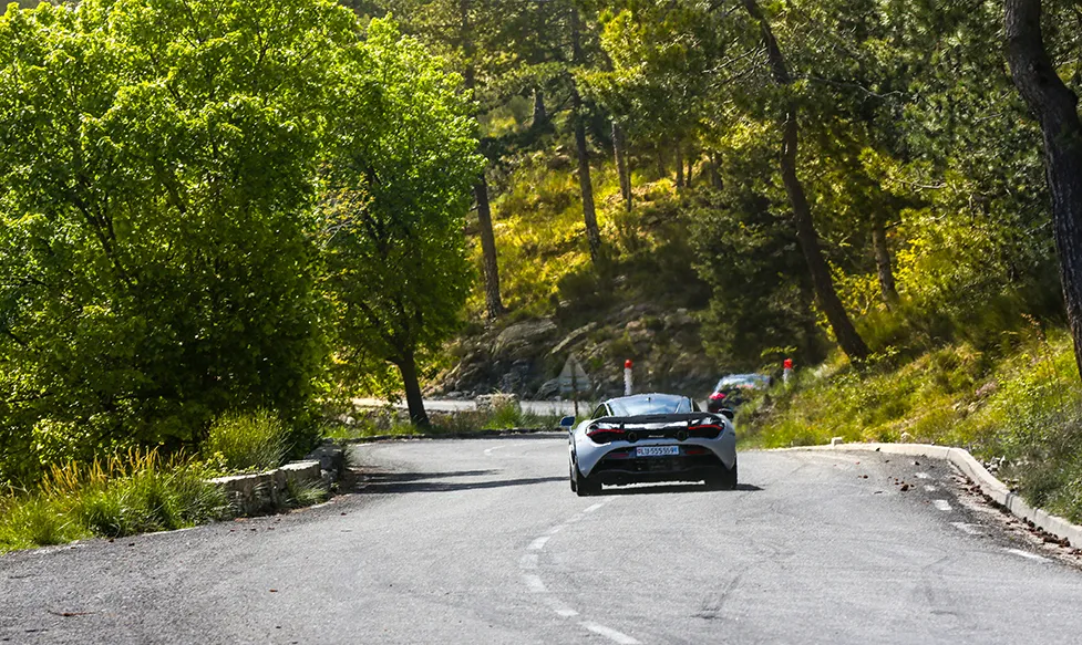 A McLaren 720S tackles a sweeping stretch of road with trees on either side on the European supercar tour