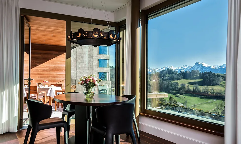 A view over green fields leading to snow capped mountains seen from a dining room at Bürgenstock Hotel